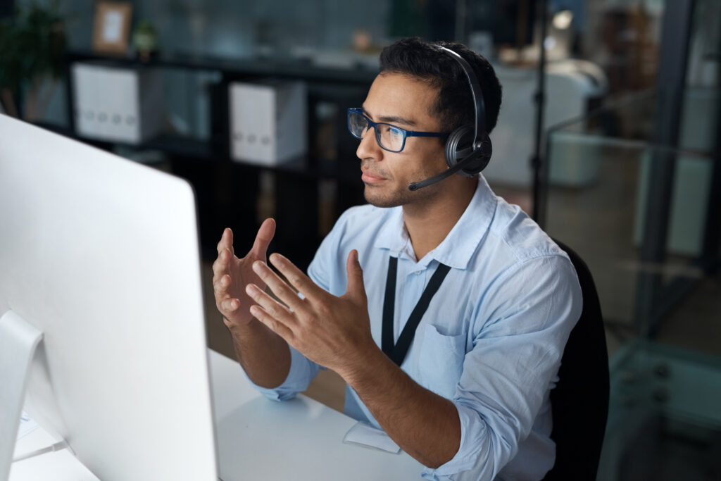 Shot of a young man using a headset and computer in a modern office